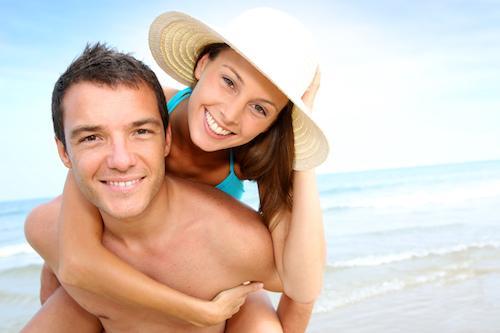 Couple smiling on the beach while wearing Invisalign clear aligners