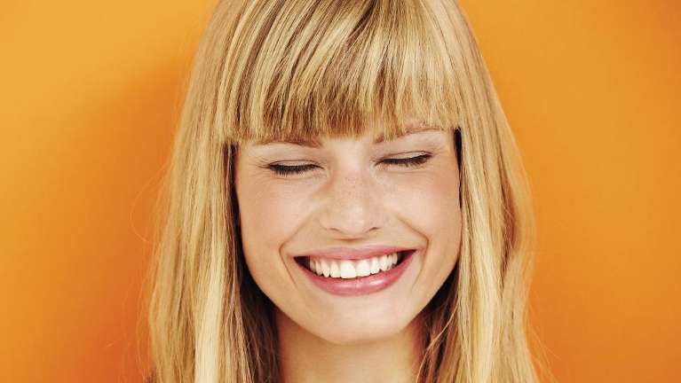 Woman smiling against orange wall at cosmetic dentist Rockville, MD